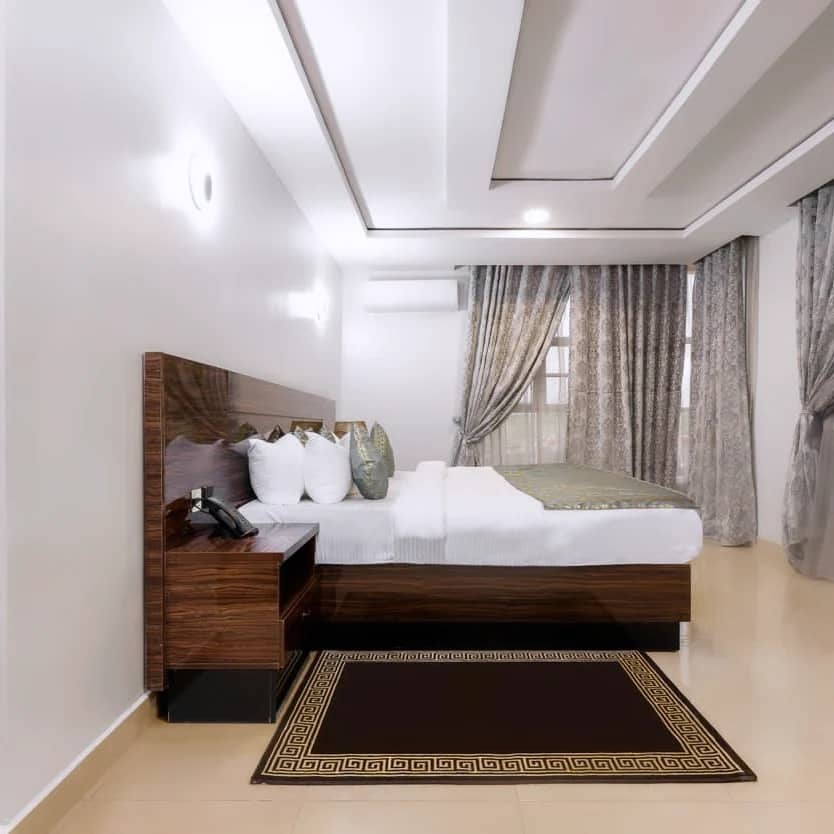 Interior view of Aveon Hotel executive suite room featuring bed, nightstand, curtains and decorative rug